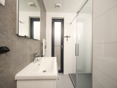 Baño moderno con ducha, lavabo y ventana en Tiny Lodge con jacuzzi en Veluwepark de Bosgraaf, Países Bajos.