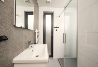 Baño moderno con ducha, lavabo y ventana en Tiny Lodge con jacuzzi en Veluwepark de Bosgraaf, Países Bajos.