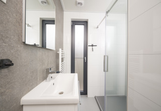 Modern bathroom with shower, sink, and window at Tiny Lodge with hot tub, Veluwepark de Bosgraaf, Netherlands.