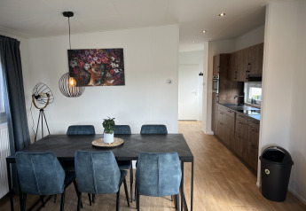 Comedor moderno con sillas azules y cocina en un chalet de Vakantiepark de Zeeuwse Parel, Países Bajos.