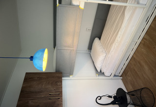 Habitación de chalet moderna con litera, lámpara azul, armario y suelo de madera en Vakantiepark de Zeeuwse Parel.