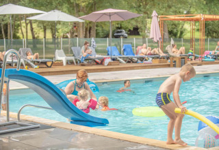 Familier nyder swimmingpoolen i Club Les Ormes feriepark med rutsjebane og solsenge i baggrunden.