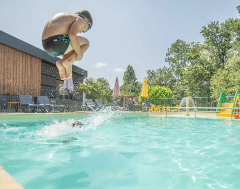 Dreng hopper i poolen med cannonball-spring på Club Les Ormes feriepark, Nouvelle-Aquitaine, Frankrig.