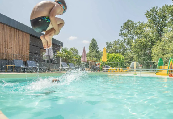 Dreng hopper i poolen med cannonball-spring på Club Les Ormes feriepark, Nouvelle-Aquitaine, Frankrig.