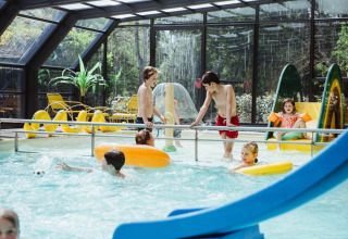 Kinder spielen im überdachten Pool mit Rutsche im Club Les Ormes, einem Ferienpark in Nouvelle-Aquitaine, Frankreich.