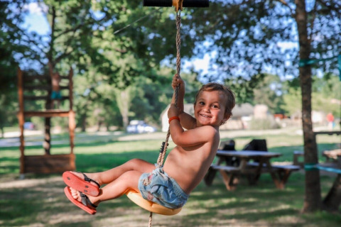 Bambino sorridente si dondola su una corda all'aperto al Club Les Ormes, Nouvelle-Aquitaine, Francia.