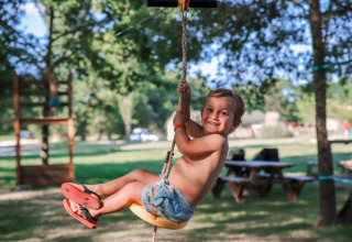 Bambino sorridente si dondola su una corda all'aperto al Club Les Ormes, Nouvelle-Aquitaine, Francia.