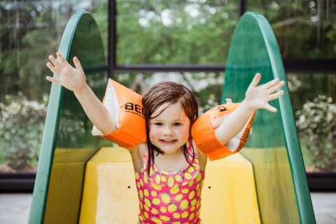Una bambina sorridente con i braccioli arancioni gioca su uno scivolo a Club Les Ormes, Nouvelle-Aquitaine, Francia.
