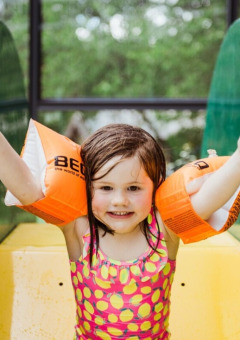 En glad pige i badedragt med orange armvinger leger på en rutsjebane i Club Les Ormes, Nouvelle-Aquitaine, Frankrig.