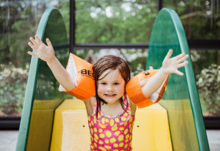 Una bambina sorridente con i braccioli arancioni gioca su uno scivolo a Club Les Ormes, Nouvelle-Aquitaine, Francia.