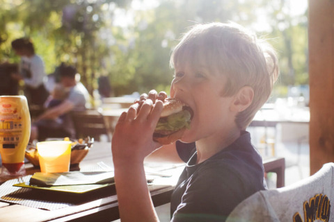 Dreng nyder en burger ved et udendørs bord på Club Les Ormes feriepark i Nouvelle-Aquitaine, Frankrig.