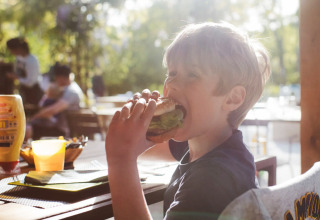 Ein Junge isst einen Burger an einem Außentisch im Club Les Ormes Ferienpark in Nouvelle-Aquitaine, Frankreich.