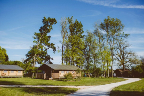 Club Les Ormes holiday park in Nouvelle-Aquitaine, France, with safari tents and tall trees under blue sky.