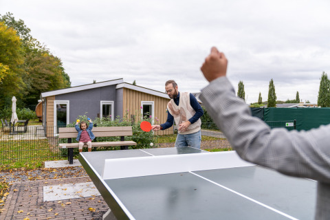 Twee mannen spelen tafeltennis buiten bij Berg Lodge - Sauna op Resort Mooi Bemelen in Nederland, met een kind op een bank.