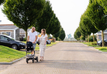 Paar mit Kinderwagen spaziert bei Berg Lodge - Sauna im Resort Mooi Bemelen, Niederlande.