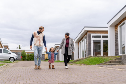Familia caminando cerca de las cabañas en Berg Lodge - Sauna en Resort Mooi Bemelen, Países Bajos, día nublado.