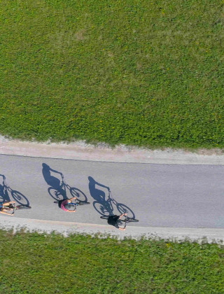 Fire cyklister på en snoet vej omgivet af grønt græs nær St Etienne de Villeréal, Nouvelle-Aquitaine, Frankrig.