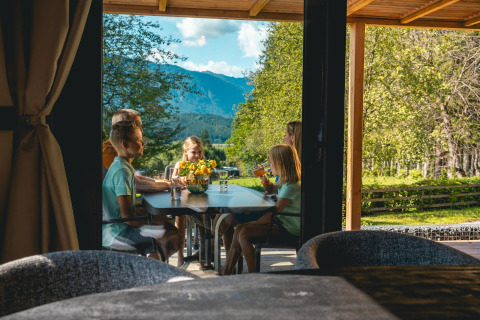 Famille partageant un repas en terrasse à la Panorama Lodge, Pressegger See, Autriche, avec vue sur la montagne.