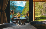 Famille partageant un repas en terrasse à la Panorama Lodge, Pressegger See, Autriche, avec vue sur la montagne.