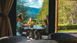 Gezin geniet van een maaltijd op het terras van Panorama Lodge aan Pressegger See, Oostenrijk, met bergzicht.