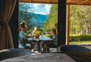 Famille partageant un repas en terrasse à la Panorama Lodge, Pressegger See, Autriche, avec vue sur la montagne.