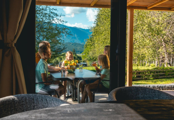 Gezin geniet van een maaltijd op het terras van Panorama Lodge aan Pressegger See, Oostenrijk, met bergzicht.