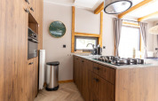 Cocina moderna de madera con estufa de gas, reloj de pared y grandes ventanas en Panorama Lodge, Pressegger See, Austria.