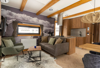 Salon moderne à la Panorama Lodge avec fresque murale de montagne, poutres apparentes et cuisine ouverte.
