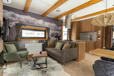 Moderne woonkamer in Panorama Lodge met bergmuurschildering, houten balken en open keukenruimte.