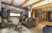 Hedendaagse zithoek in Panorama Lodge met bergmuurschildering, houten balken en open keuken.