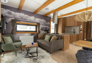 Moderne woonkamer in Panorama Lodge met bergmuurschildering, houten balken en open keukenruimte.