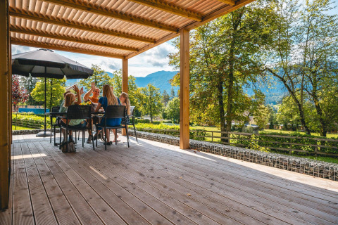 Famille partageant un repas en plein air à la Panorama Lodge, Pressegger See, Autriche, avec vue sur la montagne.