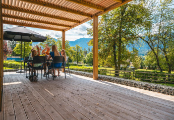Famille partageant un repas en plein air à la Panorama Lodge, Pressegger See, Autriche, avec vue sur la montagne.