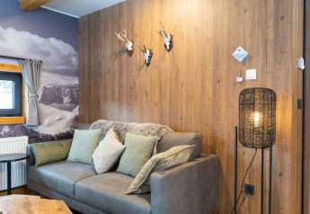 Salon à Panorama Lodge Pressegger See, Autriche, avec murs en bois, canapé, coussins, lampe et vue sur la montagne.