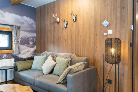 Salon à Panorama Lodge Pressegger See, Autriche, avec murs en bois, canapé, coussins, lampe et vue sur la montagne.