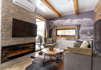 Acogedora sala de estar en Panorama Lodge en Pressegger See, Austria, con chimenea, televisor y vistas a las montañas.