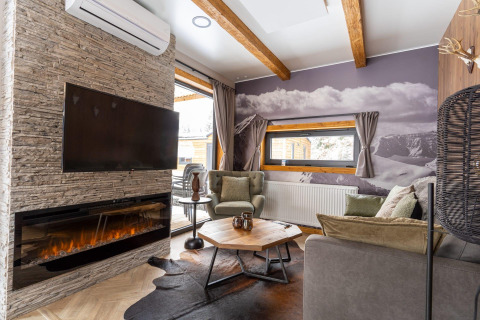 Acogedora sala de estar en Panorama Lodge en Pressegger See, Austria, con chimenea, televisor y vistas a las montañas.