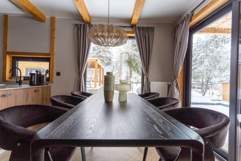 Essbereich mit Holzbalken, großen Fenstern und Blick auf verschneite Landschaft in der Panorama Lodge.