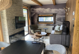 Soggiorno moderno con camino, TV, divano e poltrone presso Panorama Lodge sul lago Pressegger See in Austria.