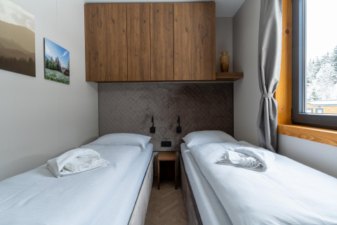 Habitación doble moderna en Panorama Lodge con dos camas individuales, armario de madera y ventana grande.