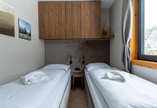Habitación doble moderna en Panorama Lodge con dos camas individuales, armario de madera y ventana grande.