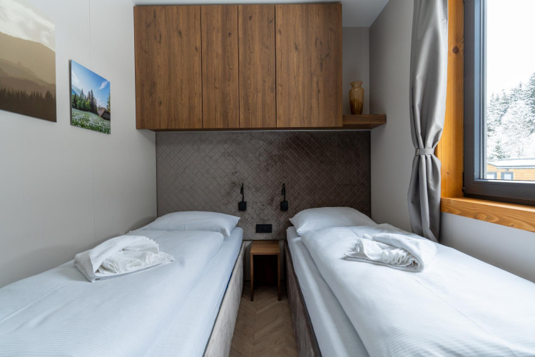 Modern twin bedroom at Panorama Lodge with wooden cabinets, large window, and scenic outdoor view.