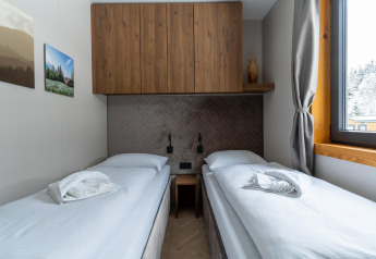 Modern twin bedroom at Panorama Lodge with wooden cabinets, large window, and scenic outdoor view.
