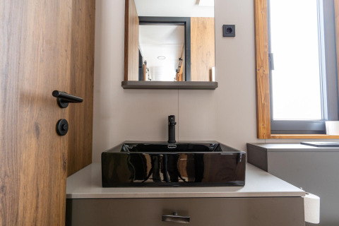 Moderne badkamer in Panorama Lodge met zwarte vierkante wastafel, houten deur en groot raam.