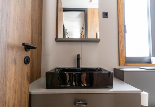Moderne badkamer in Panorama Lodge met zwarte vierkante wastafel, houten deur en groot raam.