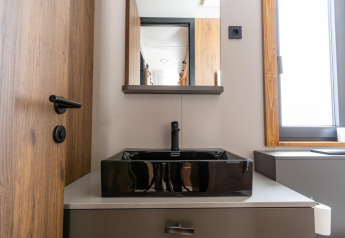 Baño moderno en Panorama Lodge con lavabo cuadrado negro, puerta de madera y ventana luminosa.