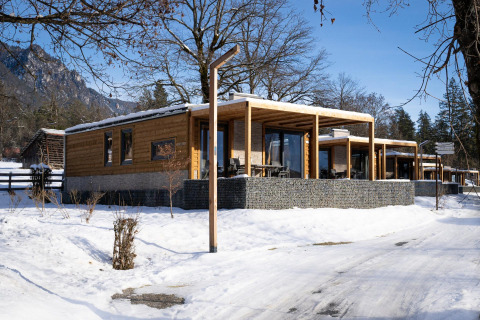 Panorama Lodge-hutten in een besneeuwd winterlandschap, met uitzicht op bergen en een heldere blauwe lucht.
