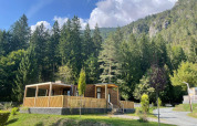 Wooden cabin at Panorama Lodge near Pressegger See, Austria, surrounded by forest and mountains on a sunny day.