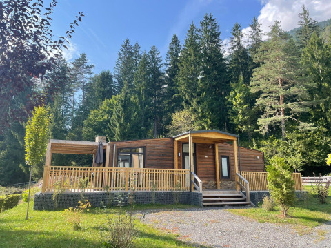 Cabane en bois au Panorama Lodge, Pressegger See, Autriche, entourée de forêt et ciel bleu.