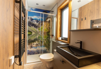 Modernes Badezimmer in der Panorama Lodge am Pressegger See mit Bergmotiv in der Dusche und Naturholz.